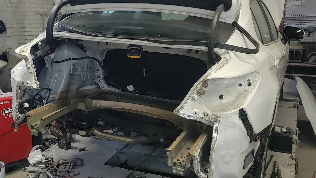 White sedan on the frame rack with its rear structure stripped for collision repair at Mickey's Auto Body in Kearny, NJ