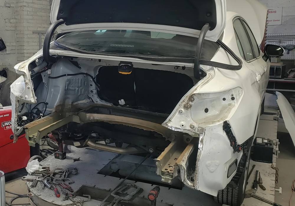 White sedan on the frame rack with its rear structure stripped for collision repair at Mickey's Auto Body in Kearny, NJ