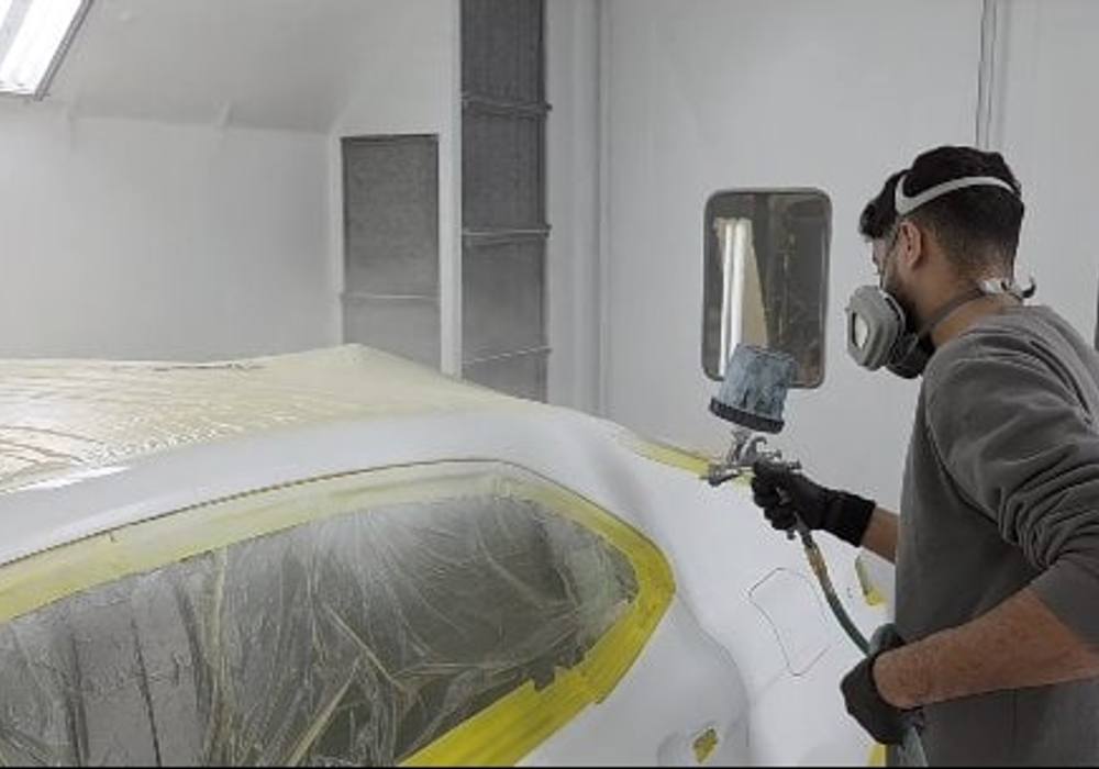 Technician in a respirator spraying a masked car in the paint booth at Mickey's Auto Body in Kearny, NJ