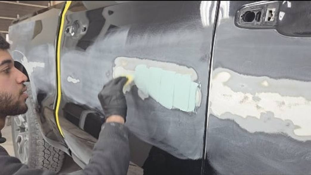 Technician applying body filler to a commercial truck door at Mickey's Auto Body in Kearny, NJ